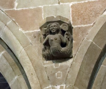 14th century corbel sculpture with a mermaid holding a mirror and comb
